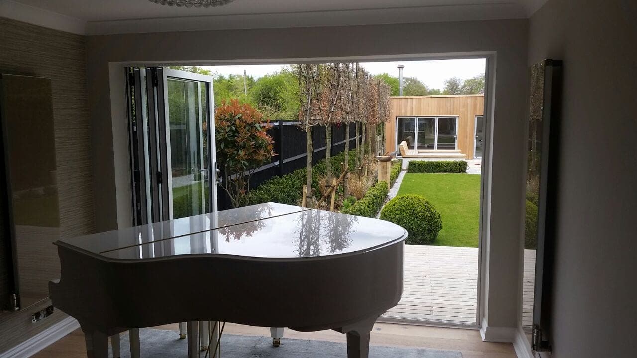 Aluminium bifold doors opening onto a garden from a family home with grand piano